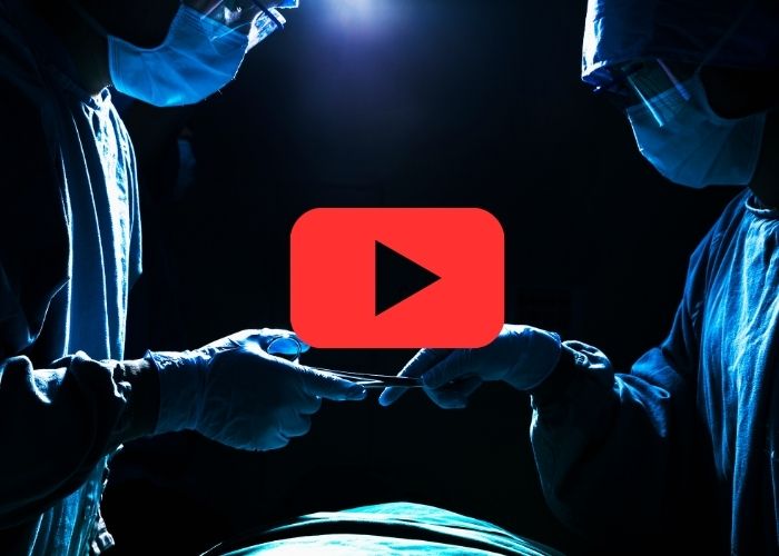 Dois cirurgiões em uma sala de cirurgia, passando um instrumento cirúrgico sob iluminação intensa, com ícone do YouTube no centro da imagem.