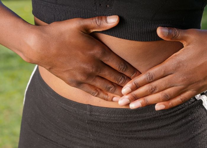 Pessoa em roupa de academia coloca as mãos sobre o abdômen, indicando desconforto na região.