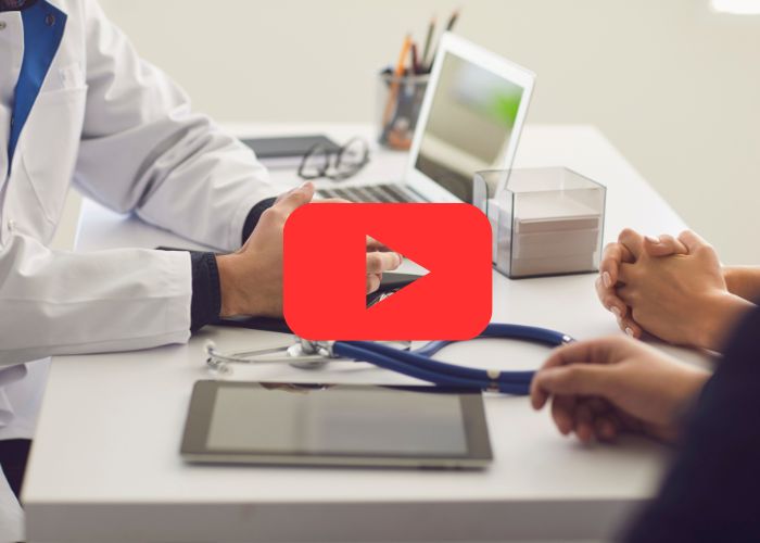 Médico conversa com paciente em consultório com estetoscópio e tablet sobre a mesa.
