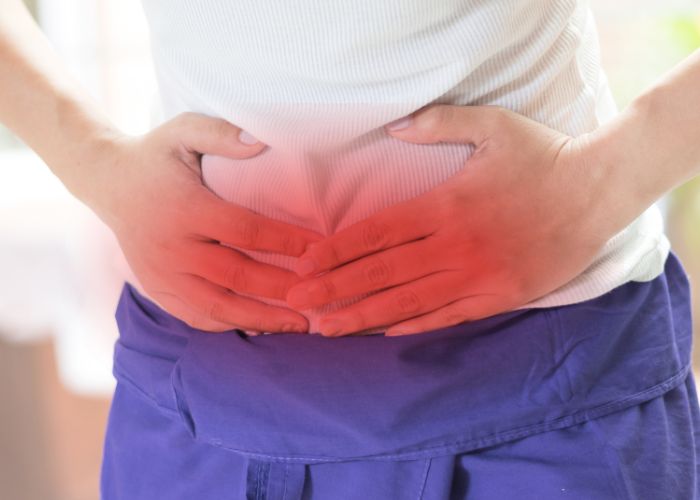 Pessoa com as mãos sobre a região abdominal inferior, destacada em vermelho, indicando dor ou desconforto abdominal.