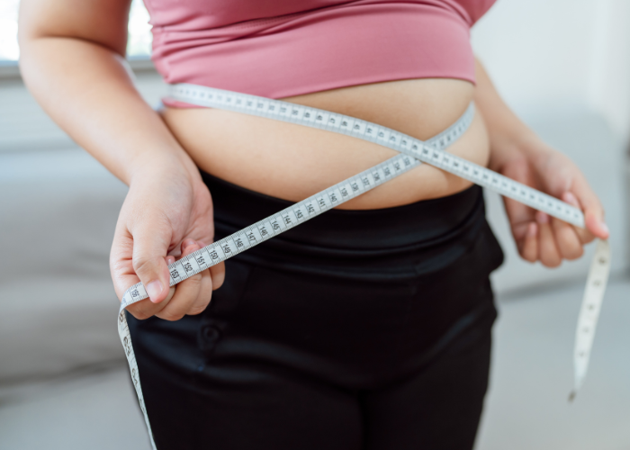 Pessoa mede a circunferência da cintura com fita métrica, evidenciando sobrepeso ou obesidade.
