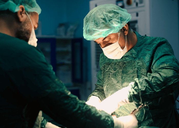 Cirurgiões em centro cirúrgico realizando procedimento, com foco no médico iluminado pelo campo operatório.