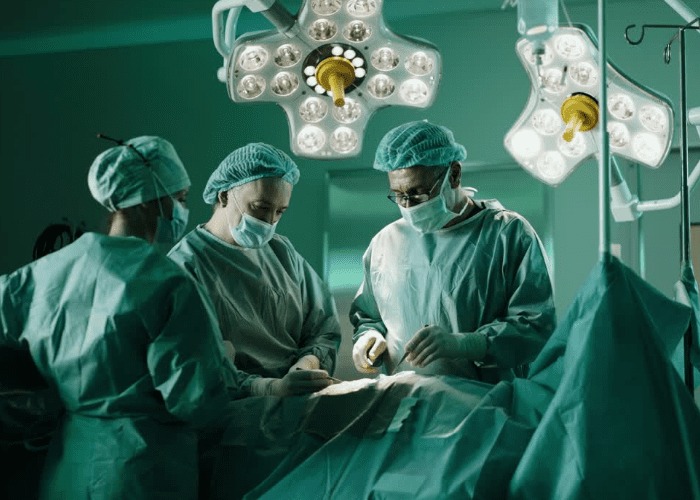 Equipe médica realizando cirurgia abdominal em centro cirúrgico, com iluminação focada e profissionais paramentados.