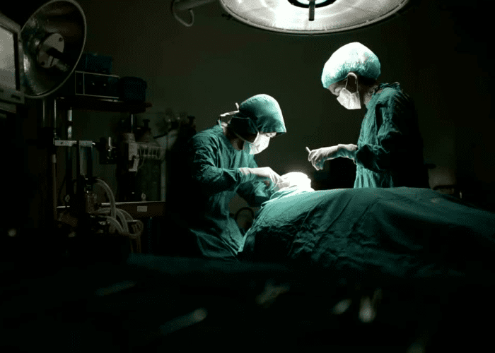 Equipe médica realiza procedimento cirúrgico em centro cirúrgico, com profissionais paramentados e foco no paciente sob iluminação hospitalar.
