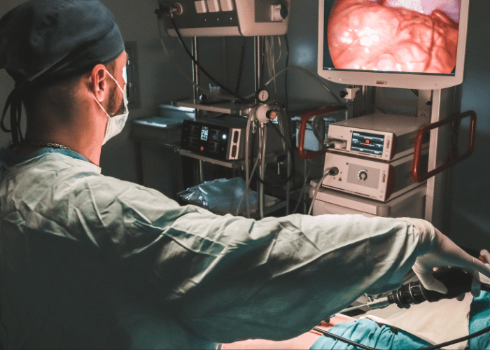 Cirurgião realiza procedimento minimamente invasivo com equipamento endoscópico em sala cirúrgica, observando monitor com imagem interna.