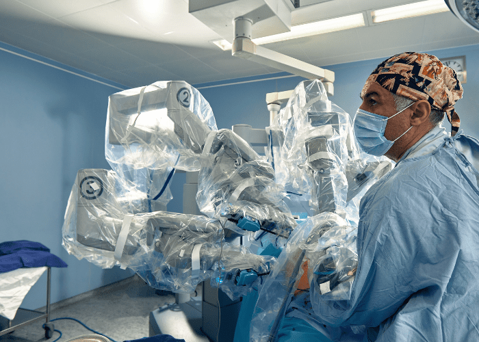 Cirurgião em sala operatória opera sistema robótico durante procedimento minimamente invasivo.