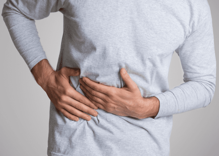 Homem segura a lateral do abdômen com as mãos, indicando dor ou desconforto na região abdominal.