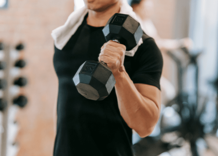 Homem realizando exercício com halter em academia, representando atividade física intensa, fortalecimento muscular e treino de força.