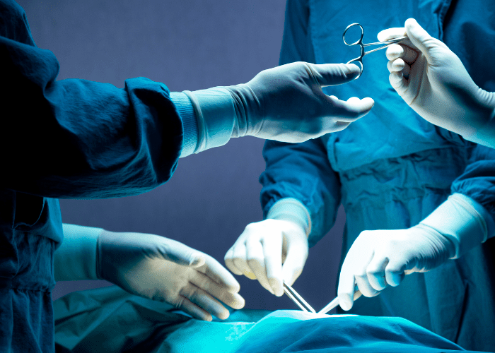 Equipe médica realizando procedimento cirúrgico em centro cirúrgico, com profissionais paramentados manipulando instrumentos durante a cirurgia.