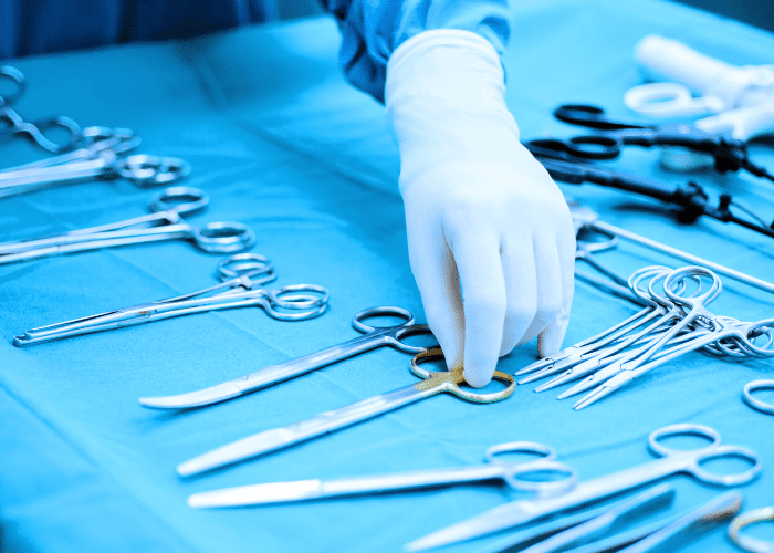 Mão de profissional de saúde selecionando instrumentos cirúrgicos esterilizados em mesa cirúrgica, representando preparo para cirurgia de hérnia.