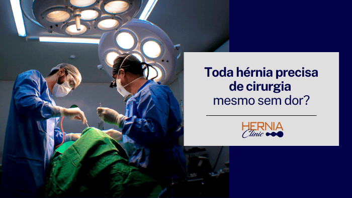 Toda hérnia precisa de cirurgia mesmo sem dor? 1 Dois cirurgiões paramentados realizando procedimento em centro cirúrgico, utilizando máscaras, luvas e instrumentos cirúrgicos sob foco de iluminação cirúrgica.